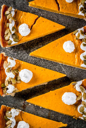 Traditional autumn dishes. Halloween, Thanksgiving. Set of cuted pieces of spicy pumpkin pie with whipped cream & pumpkin seeds on black stone table. Top viewの写真素材
