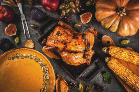 Thanksgiving Day food. Roasted whole chicken or turkey with autumn vegetables and fruits: corn, pumpkin, pumpkin pie, figs, apples, on dark grey background, top view  copy spaceの写真素材