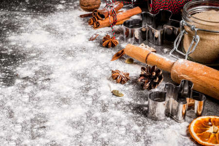 Christmas, New Year holiday cooking background. Ingredients, spices, dried oranges and baking molds, Christmas decorations (balls, fir-tree branch, cones), On black stone table, copy spaceの写真素材