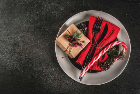 Christmas table setting with candy cane, christmas tree, pine cones and gift, on black stone table,...