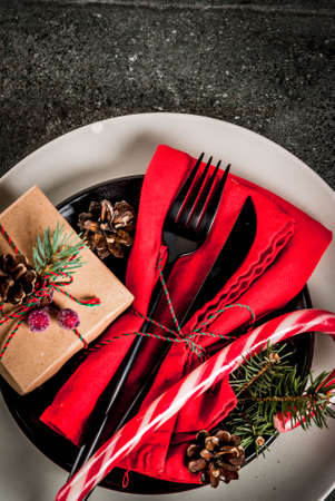 Christmas table setting with candy cane, christmas tree, pine cones and gift, on black stone table,...
