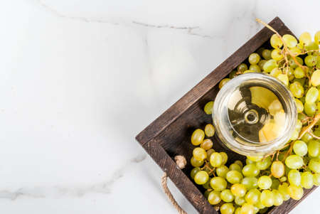 White grapes and white wine in a glass, in a wooden tray on a white marble table. Copy space top viewの写真素材