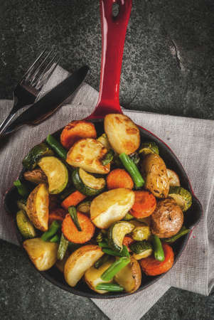 Skillet with  fried seasonal autumn vegetables (zucchini, potatoes, carrots, beans), on black stone table copy space top viewの写真素材