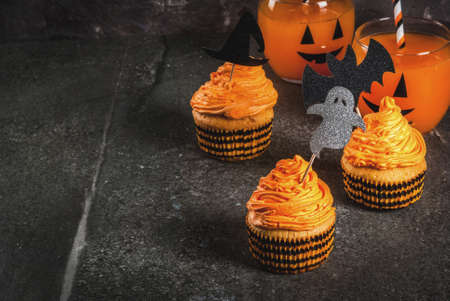 Simple idea of funny kid's treat for Halloween: pumpkin cakes with cream, with decorations in the form of holiday symbols - ghost, witch, bat. On a black background, copy spaceの写真素材
