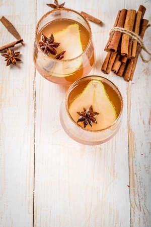 Autumn drinks. Mulled wine. Traditional autumn spicy cocktail with pear, cider and chocolate syrup, with cinnamon, anise, brown sugar. On a white wooden table. Copy spaceの写真素材