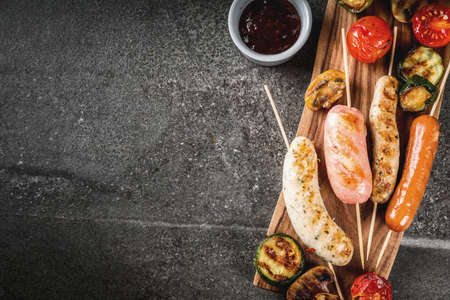 Barbecue. Assortment of various grilled meat sausages, with vegetables BBQ - mushrooms, tomatoes, zucchini, onions. On a black stone table, on cutting board plate, with sauce. Copy space top viewの写真素材