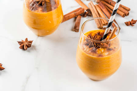 Traditional autumn dishes, spicy pumpkin pie smoothie with cinnamon, anise and oatmeal. In portioned glasses, on white marble table. Copy spaceの写真素材