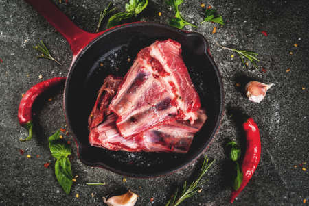 Raw fresh meat, uncooked lamb or beef ribs with hot pepper, garlic and spices in frying pan skillet on dark stone background, copy space top viewの写真素材