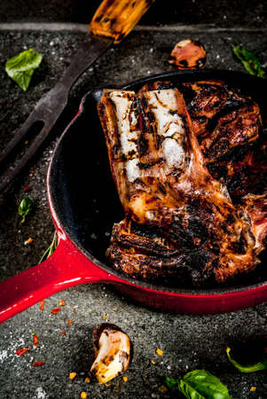 Raw fresh meat, roasted or grilled lamb or beef ribs with red tomato sauce, hot pepper, garlic and spices in skillet on dark stone background, copy spaceの写真素材