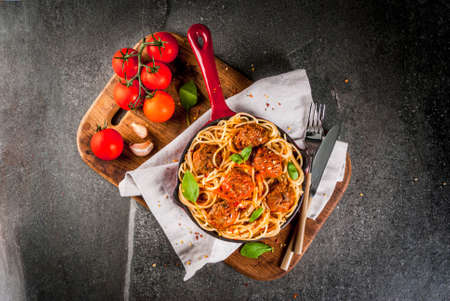 Spaghetti pasta with meatballs, basil tomato sauce in red cast iron pan, on black stone table with cutting board copy space top viewの写真素材