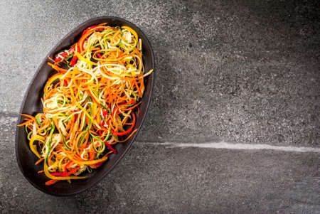 Vegan food, diet. Vegetable noodles, pasta from carrot, zucchini, bell pepper. Ready for baking cooking on a stone table. Copy space top viewの写真素材
