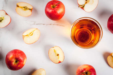Fresh organic farm apple juice in glasses with raw whole and sliced red apples, on white marble...