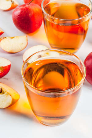 Fresh organic farm apple juice in glasses with raw whole and sliced red apples, on white marble table, copy spaceの写真素材