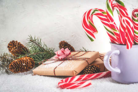 Christmas time concept, Christmas tree branches, pine cones, gifts and traditional New Year sweets candy cane, on a white marble table with snow. Copy spaceの写真素材