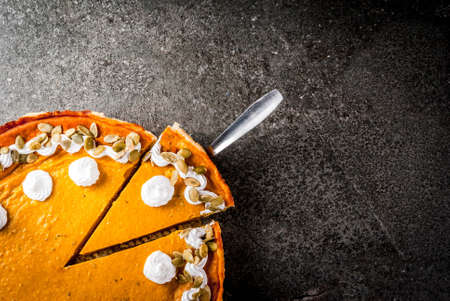 Traditional autumn dishes. Halloween, Thanksgiving. Sliced spicy pumpkin pie with whipped cream & pumpkin seeds on black stone table. Top view copy spaceの写真素材
