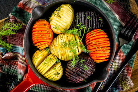 Ideas of vegan food, autumn recipes from vegetables. Roasted Hasselback Beets, carrots, potatoes, with fresh herbs, in a frying pan, on a black stone table, copy space top viewの写真素材