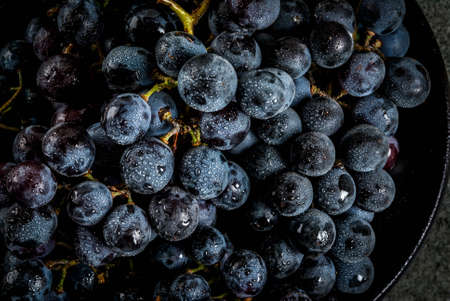 Raw natural organic farmer's black grapes, bunches on black plate, dark stone background, top close...