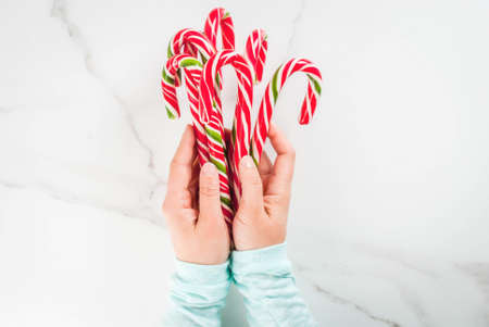 Christmas, winter concept. Holidays, sweets, treats. Girl hands holding traditional candy cane in the form of a bouquet. White marble table, top view, copy spaceの写真素材