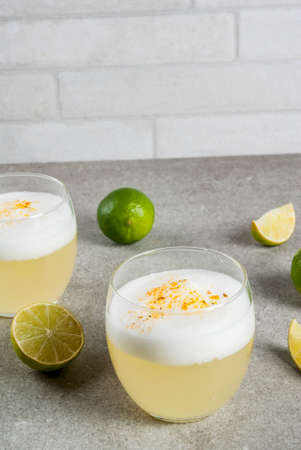 Peruvian, Mexican, Chilean traditional drink pisco sour liqueur, with fresh lime, on gray stone table, copy spaceの写真素材