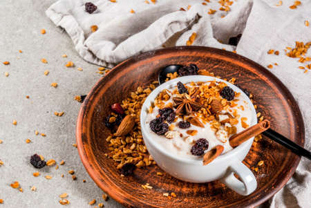 Ideas for an autumn winter breakfast. Spicy yoghurt with granola, dried berries, nuts, almonds, spices (cinnamon, anise), in cup, on plate. Gray background, copy spaceの写真素材