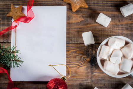 Christmas, New Year concept. Wooden table, notebook for wishlist or to do list, cocoa mug, xmas ball, pine tree, red ribbon, marshmallow. Top view copy spaceの写真素材