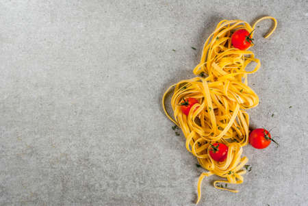 Traditional italian pasta Tagliatelle, on gray stone table with ingredients for cooking dinner - tomatoes, herbs, copy space top viewの写真素材