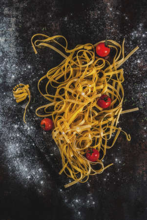 Traditional italian pasta Tagliatelle, on rusty dark metal table with ingredients for cooking dinner - tomatoes, herbs, copy space top viewの写真素材