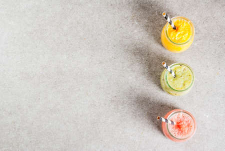 Detox organic diet drinks, homemade tropical smoothies - kiwi, orange, grapefruit, in portioned jars, on a gray stone table. Copy space top viewの写真素材