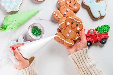 Preparation for Christmas, the girl (hands in the picture) decorates homemade hand-made traditional gingerbread with multicolored sugar icing, biscuits, white marble table. top view copy spaceの写真素材