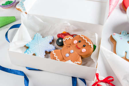 Preparing for Christmas, decorating traditional gingerbread with multicolored sugar glaze, cookies, gingerbread in a white gift box, with ribbon bow, on a white marble table copy spaceの写真素材