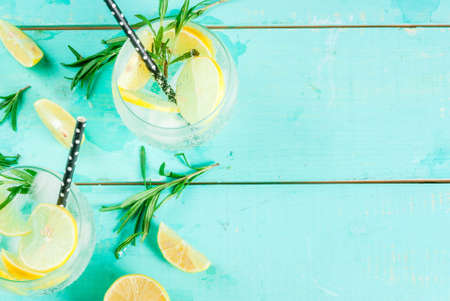 Cold lemonade or alcohol vodka cocktail with lemon and rosemary, on light blue table, copy space top viewの写真素材