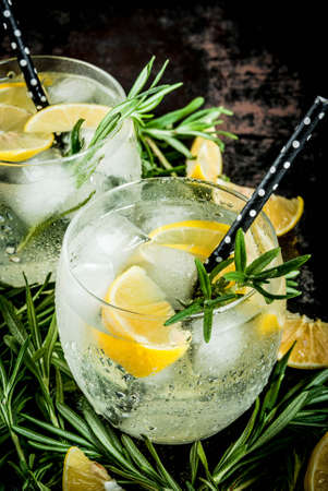 Cold lemonade or alcohol vodka cocktail with lemon and rosemary, On a black rusty metallic background, copy spaceの写真素材
