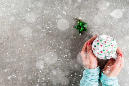 Christmas and New Year concept. Girl drinking coffee or hot chocolate, with whipped cream and sweet stars decoration, on gray stone table, hands in the picture, top view, copy space with snow effectの写真素材