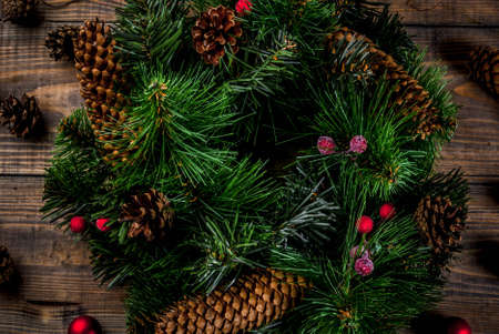 Preparation for xmas holidays. Christmas decorative green wreath with pine cones and red winter berries and christmas tree balls, wooden background, top close viewの写真素材