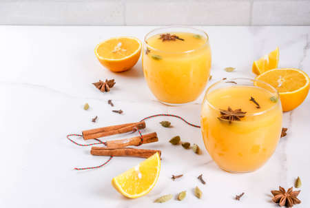 Fall, winter cocktails, Hot and spicy winter orange punch with cinnamon, anise stars, cardamom, cloves. On a white marble table, with ingredients, in glasses. Copy spaceの写真素材