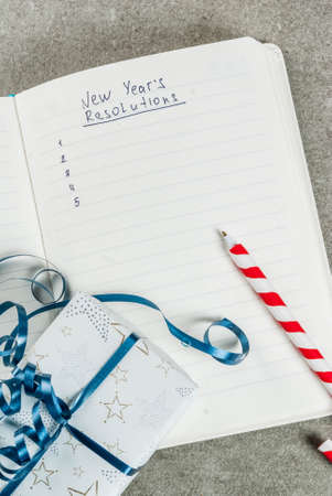 New years resolutions concept, open notebook on a grey stone table table. with christmas gift, pen and decoration and blank list. copy spaceの写真素材