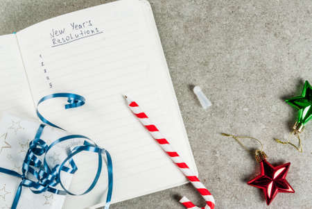 New years resolutions concept, open notebook on a grey stone table table. with christmas gift, pen...