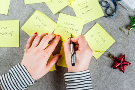 Girl writing new years resolutions, hands in picture. Grey stone table with colorful sticky notes...