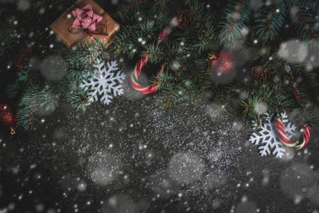 Christmas dark background with christmas tree branches, pine cones, candy cane sweets, gifts,...