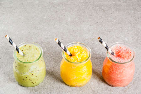 Detox organic diet drinks, homemade tropical smoothies - kiwi, orange, grapefruit, in portioned jars, on a gray stone table. Copy spaceの写真素材