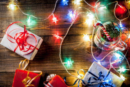 Christmas, New Year's concept. Mason Jar with decorations, fir cones, artificial snow, candy cane and fir branch. On a wooden table background, with a lit garland turned on. Copy space top view frameの写真素材