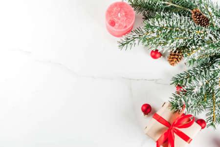 Christmas background for greeting card. Christmas tree branches with snow effect with festive red ribbon, pine cones, gift boxes and candles, on white marble background, copy space top viewの写真素材