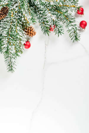Christmas background for greeting card. Christmas tree branches with snow effect with festive red ribbon, pine cones, gift boxes and candles, on white marble background, copy space top viewの写真素材