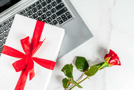 Valentine's day concept, laptop, white gift box with red ribbon and one rose flower, on white marble table, copy space top viewの写真素材