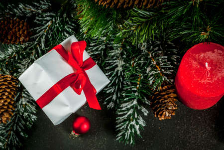 Christmas background for greeting card. Christmas tree branches with snow effect with festive red ribbon, pine cones, gift boxes and candles, on dark blue background, copy space top viewの写真素材