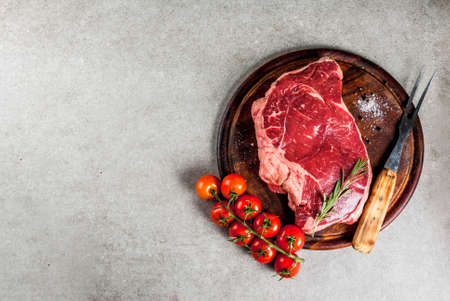 Fresh raw meat, lamb beef marble steak on a cutting board, with ingredients for cooking. On grey stone table, copy space top viewの写真素材