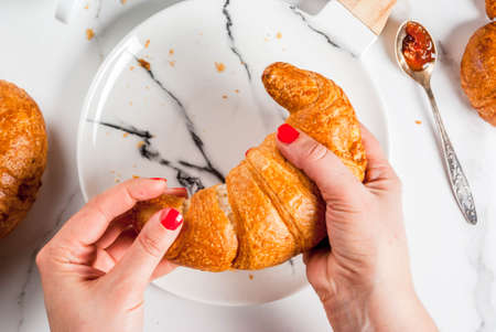 Girl eats homemade continental breakfast, croissants, coffee. jam on white marble table, copy space top view, hands in pictureの写真素材