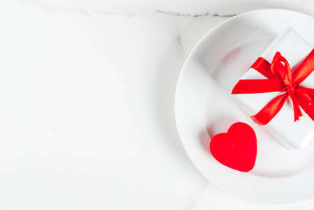 Valentine's day table setting with plate, gift box and red heart, on white marble background top view copy spaceの写真素材