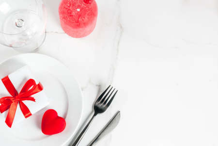 Valentine's day table setting with plate, fork, knife, gift box and red heart, on white marble background top view copy spaceの写真素材
