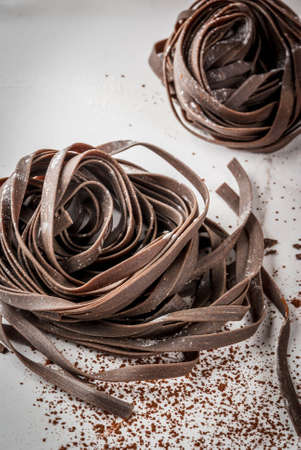 Raw unprepared chocolate pasta noodles. On a white kitchen marble table. Copy spaceの写真素材